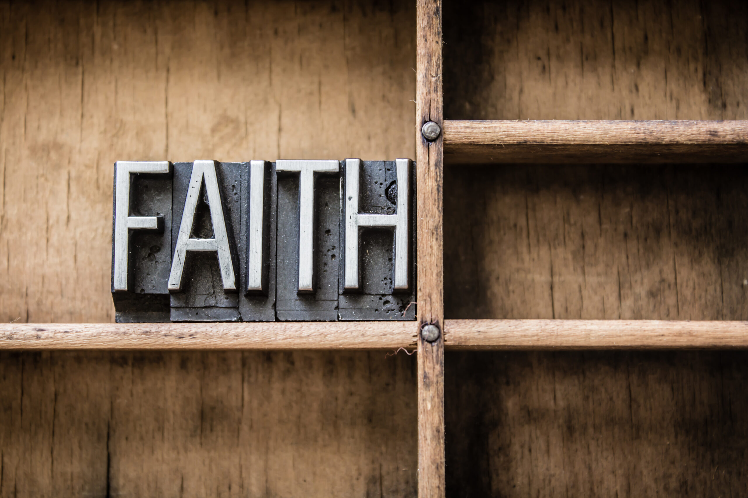 Metal type letters spell "FAITH" on a wooden shelf. The image symbolizes belief and hope, relevant for discussions on faith or inspiration.